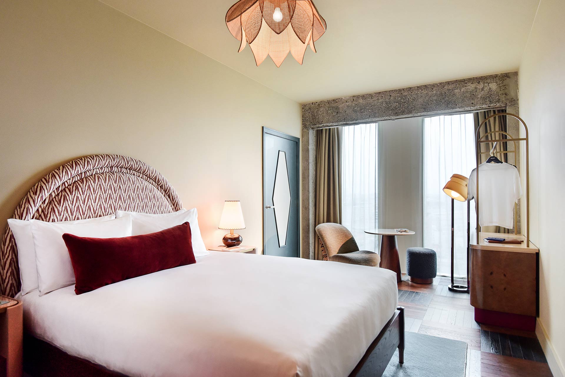 A well-lit bedroom interior with comfy bed, armchair in rear and view through the large windows.