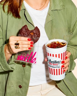 A woman holding a chocolate cookie and a fizzy drink.