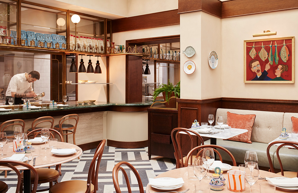 Alassio Winter interior, featuring a high, bright ceiling, décor that pays homage to Italy, and a chef at work in the kitchen.