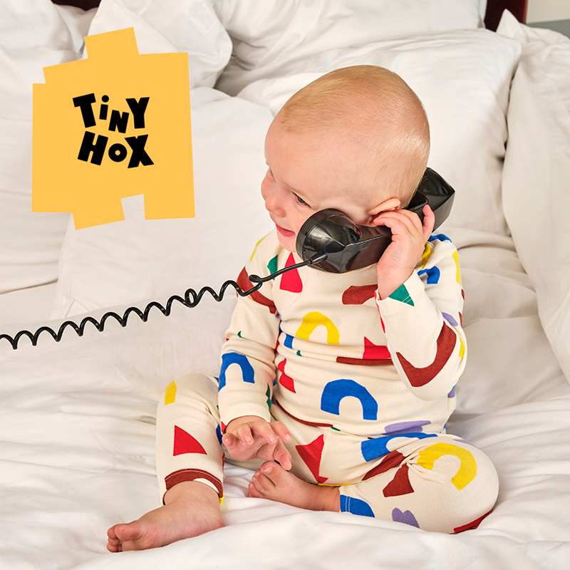 The Tiny Hox logo overlays an image of a baby answering the phone while sitting on a white mattress.
